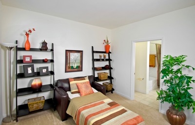 Spacious bedroom with orange decor and house plants with direct access to the bathroom.