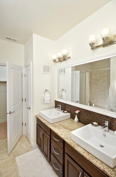 Well-lit bathroom with double vanity, tile backsplash, storage closet, and granite countertop.