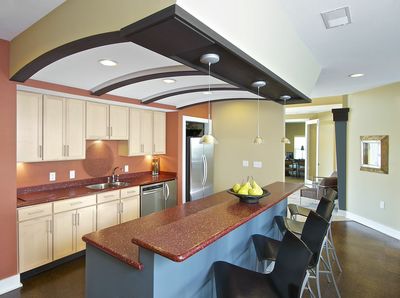 Large clubhouse kitchen with a breakfast bar, barstools, stainless steel fridge, and white finished cabinets.