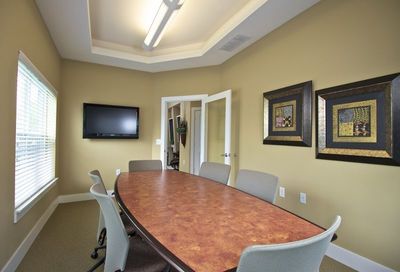 Business center conference room with a long meeting table, TV on the back wall, and photos on the righthand wall. 