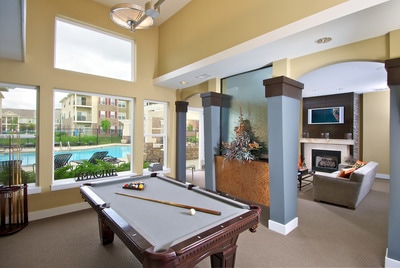 Clubhouse with a full-sized pool table and resident lounge, with the pool visible through large windows.